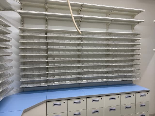 新規納品直後の調剤薬局什器 — 整然とした空棚と青カウンター